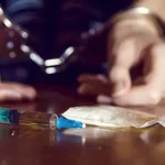 Handcuffed individual behind a syringe and packet of white powder; illustrating legal and health impacts of drug addiction.